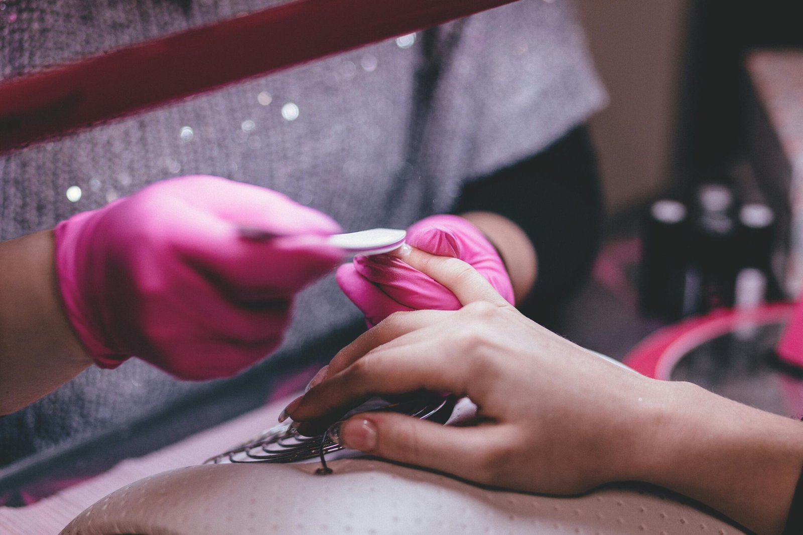 Close-up of a professional manicure session with pink gloves and a nail file in an indoor salon.
